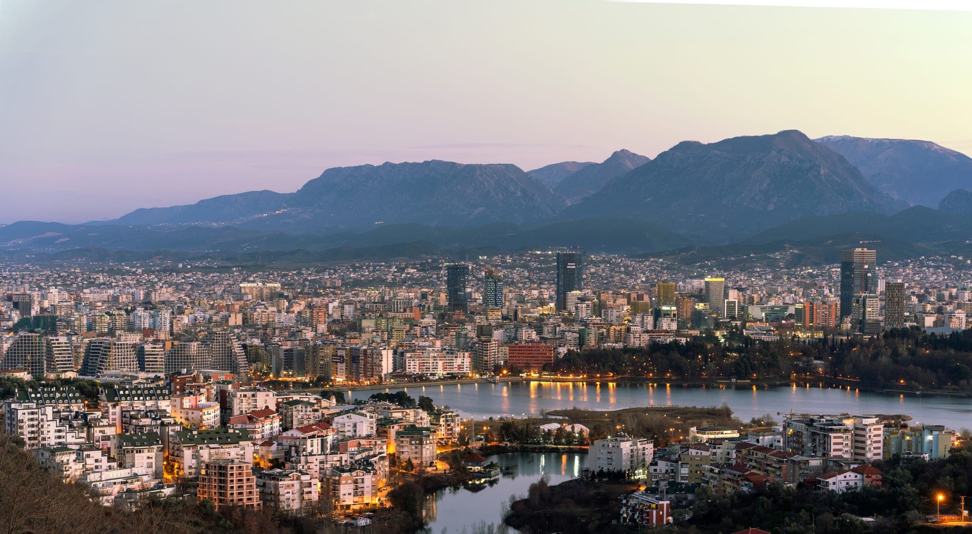 Tirana at dusk, city lights around the artificial lake with the Dajti mountains behind